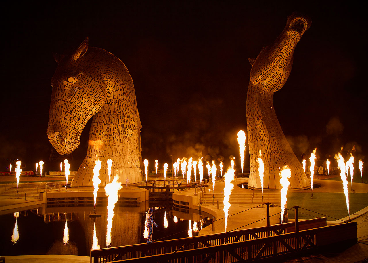 A performer balances on a handrail as flames illuminate the Kelpies during their opening ceremony, near Falkirk, Scotland.